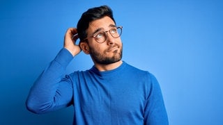 Junger Mann mit Brille und blauem Pullover schaut nachdenkend in die Luft. Symbolbild für Sätze, die du nur verstehst, wenn du Dialekt sprichst.