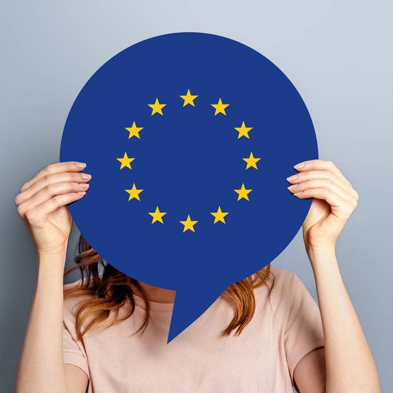Eine Frau hält eine Spprechbalse vor ihrem Gesicht hoch, auf der das Zeichen für das Europäische Parlament zu sehen ist und fragt sich, was es mit ihr zu tun hat