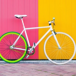 Ein weißes Fahrrad steht vor einer gelb-pinken Wand. 
