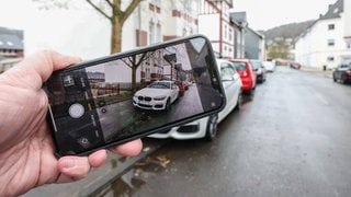 Eine Hand mit einem Smartphone fotografiert einen vermutlichen Falschparker um diesen anzuzeigen. | Symbolbild: Falschparker melden