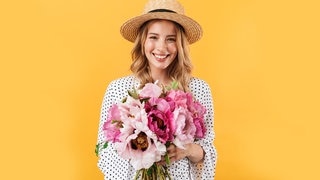 Junge Frau mit Sonnenhut und einem Strauß Blumen in der Hand. Symbolbild für Sprüche, mit denen wir es durch die Blume sagen können, offiziell freundlich.