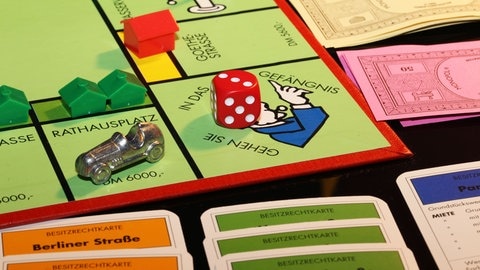 Spielfiguren, Würfel und das Spielfeld von Monopoly. Mit welchen Tricks kann man am besten gewinnen?