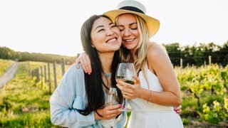 Zwei Frauen nehmen sich mit einem Glas Wein in den Arm | Symbolbild: Gibt es „guten“ Wein ohne Alkohol?