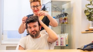 Mann schaut etwas skeptisch, während die Friseurin in seinen Haaren werkelt. Symbolbild für typische Sprüche vom Friseur, die Kunden nicht hören wollen. (Foto: IMAGO, IMAGO / imagebroker) Mann schaut etwas skeptisch, während die Friseurin in seinen Haaren werkelt. Symbolbild für typische Sprüche vom Friseur, die Kunden nicht hören wollen.