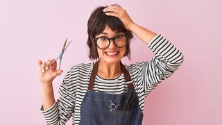 Frau mit Schere und in der Kleidung einer Friseurin. Symbolbild für typische Sprüche vom Friseur, die Kunden nicht hören wollen.
