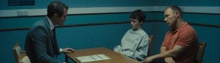 Der Hauptdarsteller der Serie „Adolescence“ sitzt an einem Tisch. Zwei Männer reden auf ihn ein.
