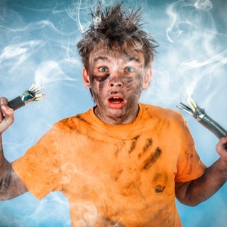 Junge hält zwei Stromkabel in der Hand, es gab eine kleine Explosion. Das Gesicht des Kindes ist voll mit Ruß und Staub. Symbolbild für die Frage: Haften Eltern für ihre Kinder oder nicht?