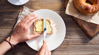 Eine Frauenhand streicht Butter auf ein Brot. Welche Vorteile Butter bei der Ernährung hat, kannst du hier lesen!
