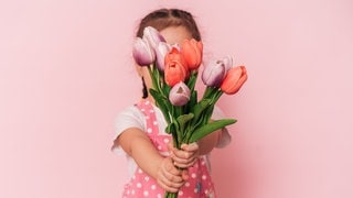 Kleines Mädchen unscharf hinter einem Strauß Tulpen. Symbolbild für lustige und schöne Whatsapp-Sprüche und Grüße an Mama zum Muttertag.