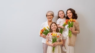 Oma, Mutter und Töchter haben Tulpen in der Hand und gratulieren sich zum Muttertag. 