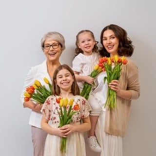 Oma, Mutter und Töchter haben Tulpen in der Hand und gratulieren sich zum Muttertag. 