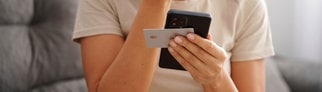 Eine junge Frau hält eine Hand vors Gesicht, in der anderen Handy und Kreditkarte. Sie ist auf einen Betrug reingefallen.