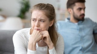 Ein Paar sitzt nebeneinander auf der Couch, beide sehen unglücklich aus mit der Beziehung