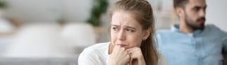 Ein Paar sitzt nebeneinander auf der Couch, beide sehen unglücklich aus mit der Beziehung