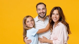Junger Vater, Tocher und Frau stehen lachend beisammen. Symbolbild für lustige Whatsapp-Sprüche für Papa am Vatertag.