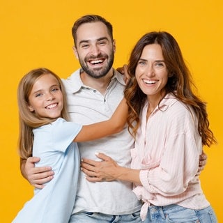 Junger Vater, Tocher und Frau stehen lachend beisammen. Symbolbild für lustige Whatsapp-Sprüche für Papa am Vatertag.