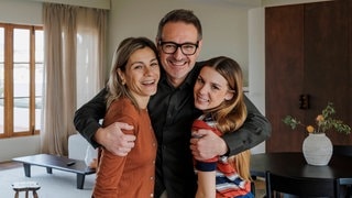 Junger Vater, Tocher und Frau stehen lachend beisammen. Symbolbild für lustige Whatsapp-Sprüche für Papa am Vatertag.