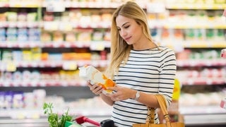 Junge Frau mit Einkaufswagen im Supermarkt. Sie schaut auf ein Tetrapak Saft. Symbolbild für Preissturz bei den Discountern: Diese Produkte sind jetzt günstiger.