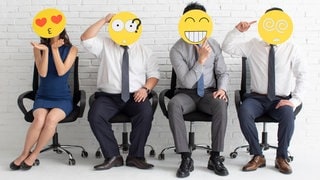 Sprüche im Büro: Kollegen im Büro sitzen nebeneinander. Sie halten Emojis vor ihr Gesicht. Im Job gibt es viele Emotionen, die durch die Emojis verkörpert werden. 