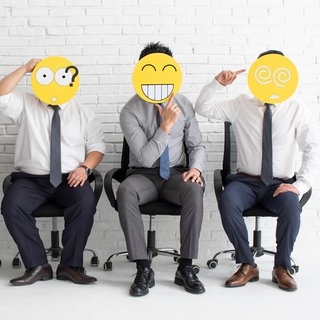 Sprüche im Büro: Kollegen im Büro sitzen nebeneinander. Sie halten Emojis vor ihr Gesicht. Im Job gibt es viele Emotionen, die durch die Emojis verkörpert werden. 