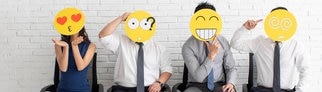 Sprüche im Büro: Kollegen im Büro sitzen nebeneinander. Sie halten Emojis vor ihr Gesicht. Im Job gibt es viele Emotionen, die durch die Emojis verkörpert werden. 