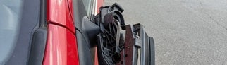 Ein Außenspiegel hängt beschädigt an einem roten Auto herunter. Betrüger zocken Autofahrer teilweise mit präparierten Außenspiegeln ab.