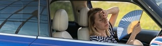 Eine Frau sitzt mit Fächer im Auto, da sie ihr Auto nicht vor Hitze geschützt hat.