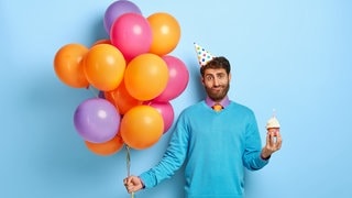 Ein Mann mit Luftballons fragt sich, was für ein Geschenk er zu einer Einladung mitbringen soll.