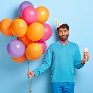 Ein Mann mit Luftballons fragt sich, was für ein Geschenk er zu einer Einladung mitbringen soll.