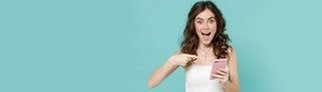 Junge Frau im Brautkleid zeigt lachend auf ihr Smartphone. Symbolbild für lustige Whatsapp-Sprüche und Glückwünsche zur Hochzeit.
