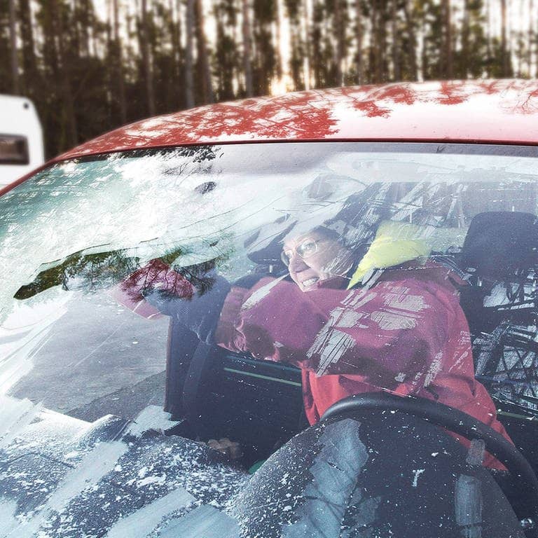 Die Innenscheibe im Auto ist gefroren und vereist. Eine Frau, dick eingepackt in Winterklamitten, kratzt die Scheibe von innen frei. (Foto: IMAGO, IMAGO / teamwork)