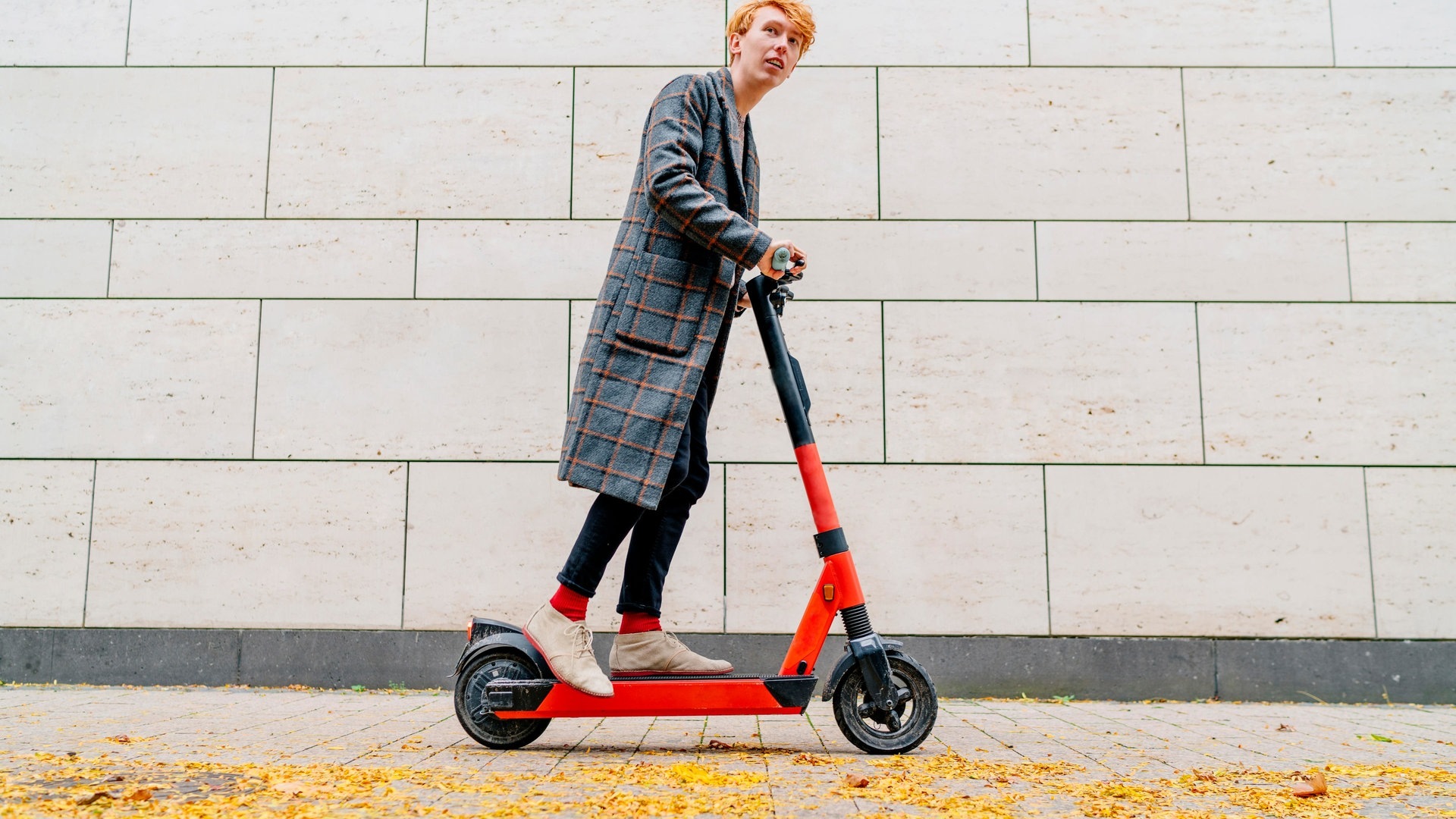 Mann mit E-Scooter auf Bürgersteig vor grauer Wand (Foto: dpa Bildfunk, Picture Alliance)