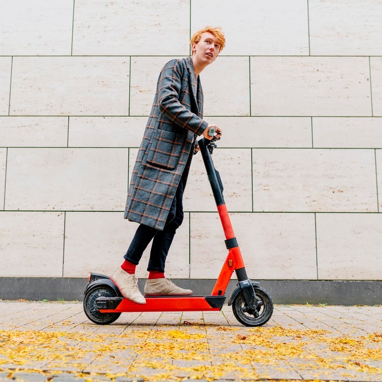 Mann mit E-Scooter auf Bürgersteig vor grauer Wand (Foto: dpa Bildfunk, Picture Alliance)