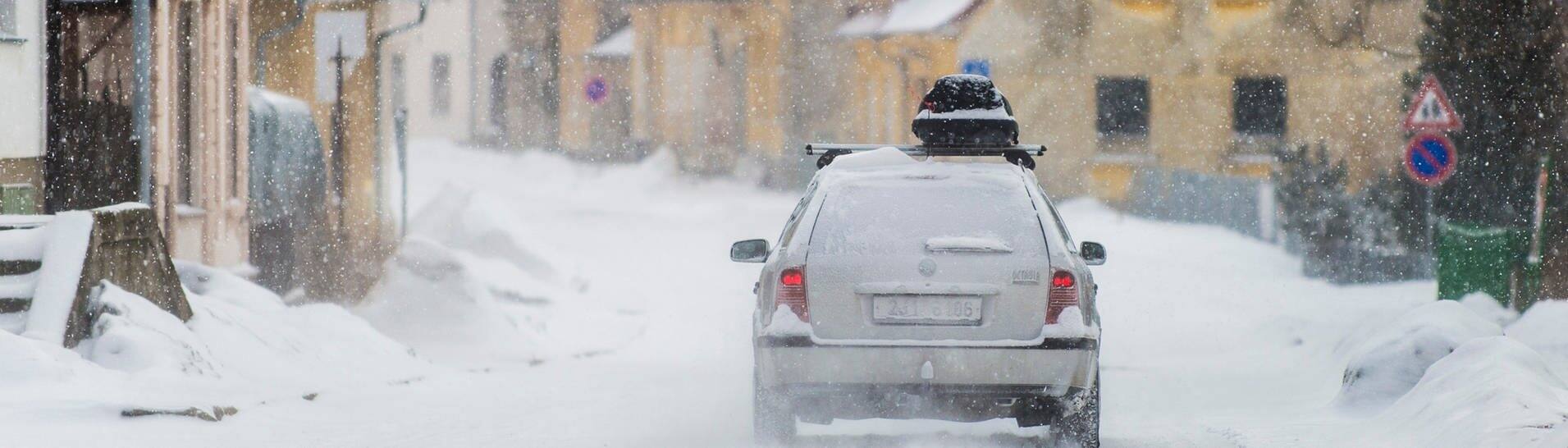 Ein Auto ist bei Schnee unterwegs in den Skiurlaub und hat eine Dachbox auf dem Dach (Foto: picture-alliance / Reportdienste, picture alliance / photothek | Florian Gaertner)