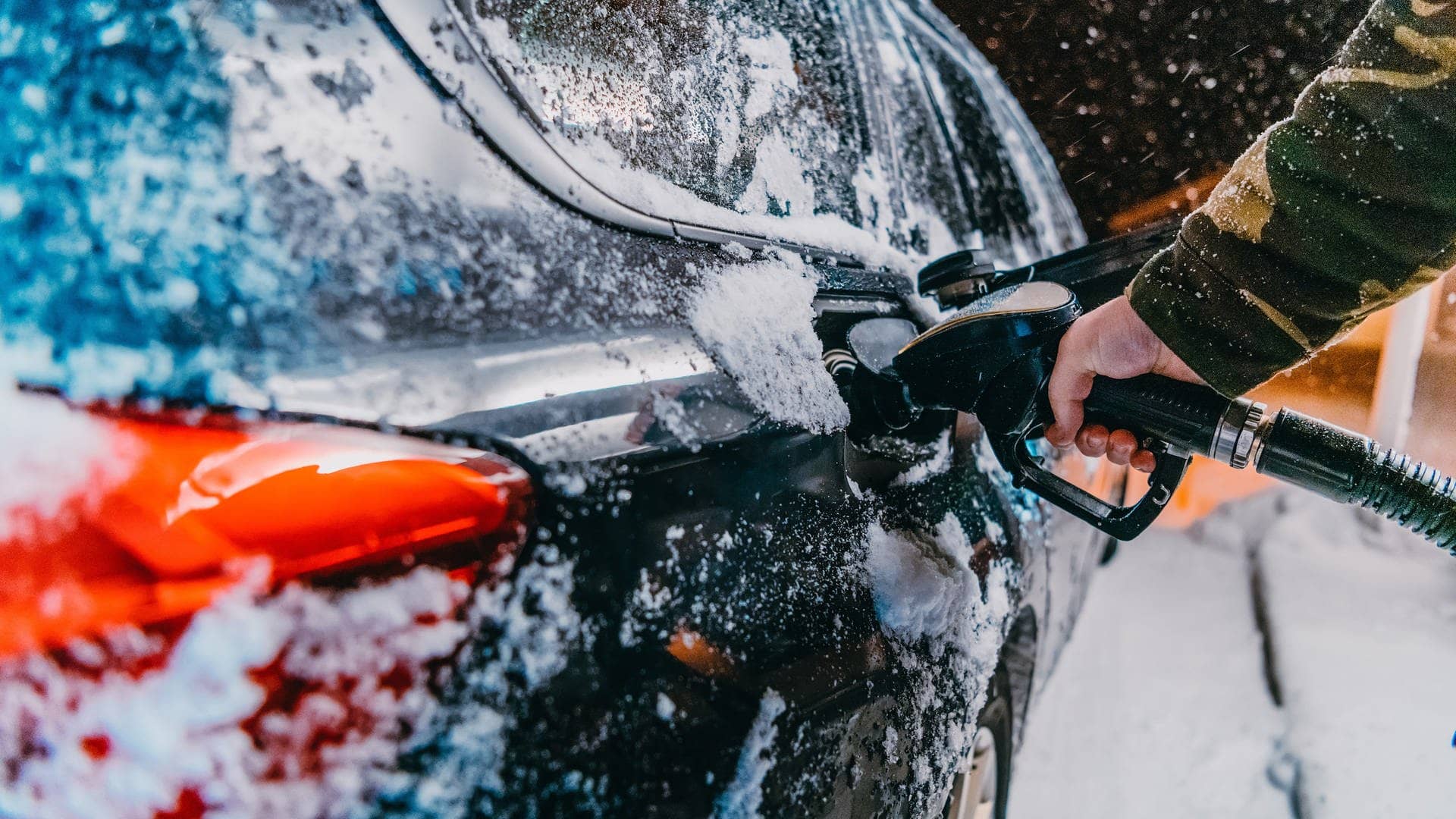 Ein schwarzes Auto wird im Winter an einer Tankstelle betankt. Es fallen Schneeflocken. Das Foto soll den erhöhten Spritverbrauch im Winter, beispielsweise auf dem Weg in den Skiurlaub, verdeutlichen. Wir klären, woran das liegt und welche Tipps es gibt, um die größtens Spritfresser im Winter zu vermeiden. (Foto: Adobe Stock, .shock)