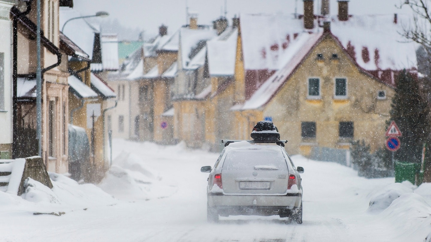 Ein Auto ist bei Schnee unterwegs in den Skiurlaub und hat eine Dachbox auf dem Dach