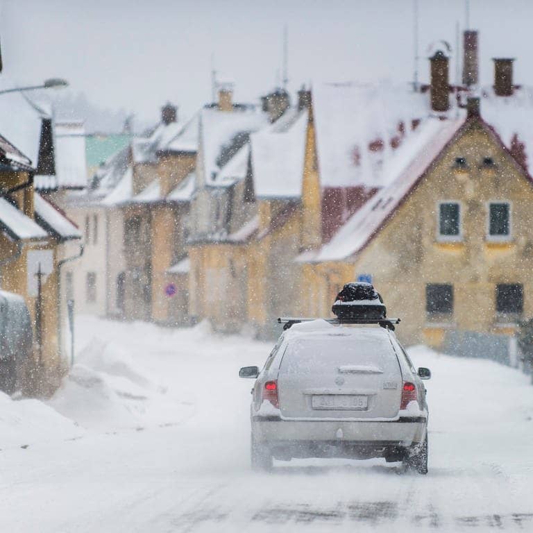 Ein Auto ist bei Schnee unterwegs in den Skiurlaub und hat eine Dachbox auf dem Dach