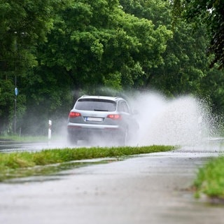Ein silbernes Auto fährt vorsichtig bei Nässe über eine überflutete Straße, denn es besteht Gefahr durch Aquaplaning