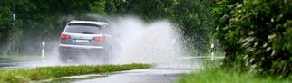 Ein silbernes Auto fährt vorsichtig bei Nässe über eine überflutete Straße, denn es besteht Gefahr durch Aquaplaning