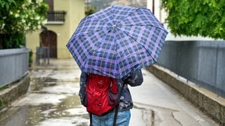 Eine Person läuft mit Regenschirm durch eine Straße in Italien. Über Ostern gibt es dort und in Spanien extremen Regen und heftige Unwetter.