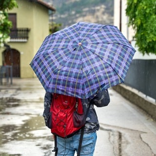 Eine Person läuft mit Regenschirm durch eine Straße in Italien. Über Ostern gibt es dort und in Spanien extremen Regen und heftige Unwetter.