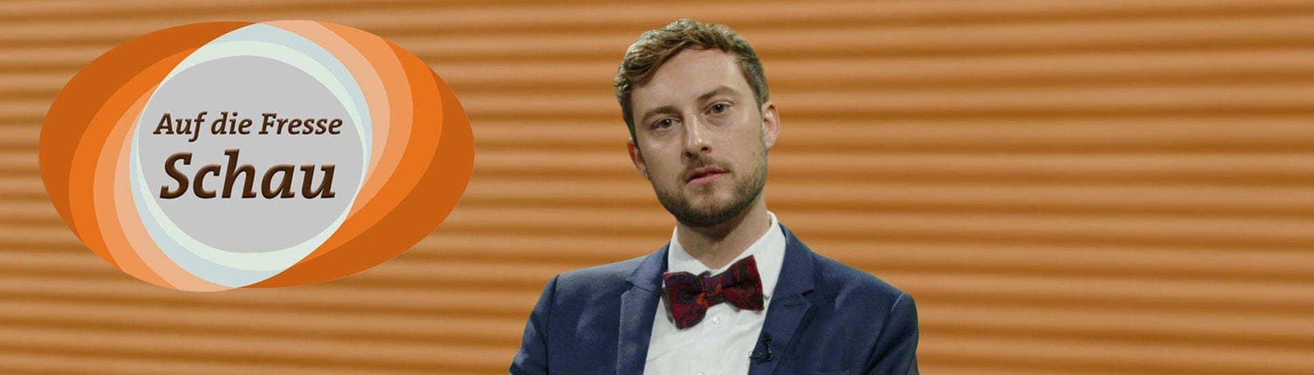 SWR3-Moderator Constantin Zöller sitzt mit Jackett in einem Fernsehstudio. Er liest Hasskommentare, das Logo der Sendung ist eingeblendet mit der Aufschrift „Auf-die-Fresse“-Schau. (Foto: SWR3)