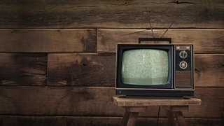 Ein altes Fernsehgerät steht vor einer holzvertäfelten Wand und ist ein Symbol fürs Älterwerden (Foto: picture-alliance / Reportdienste, picture alliance / Zoonar | Marco Martins) Ein altes Fernsehgerät steht vor einer holzvertäfelten Wand und ist ein Symbol fürs Älterwerden