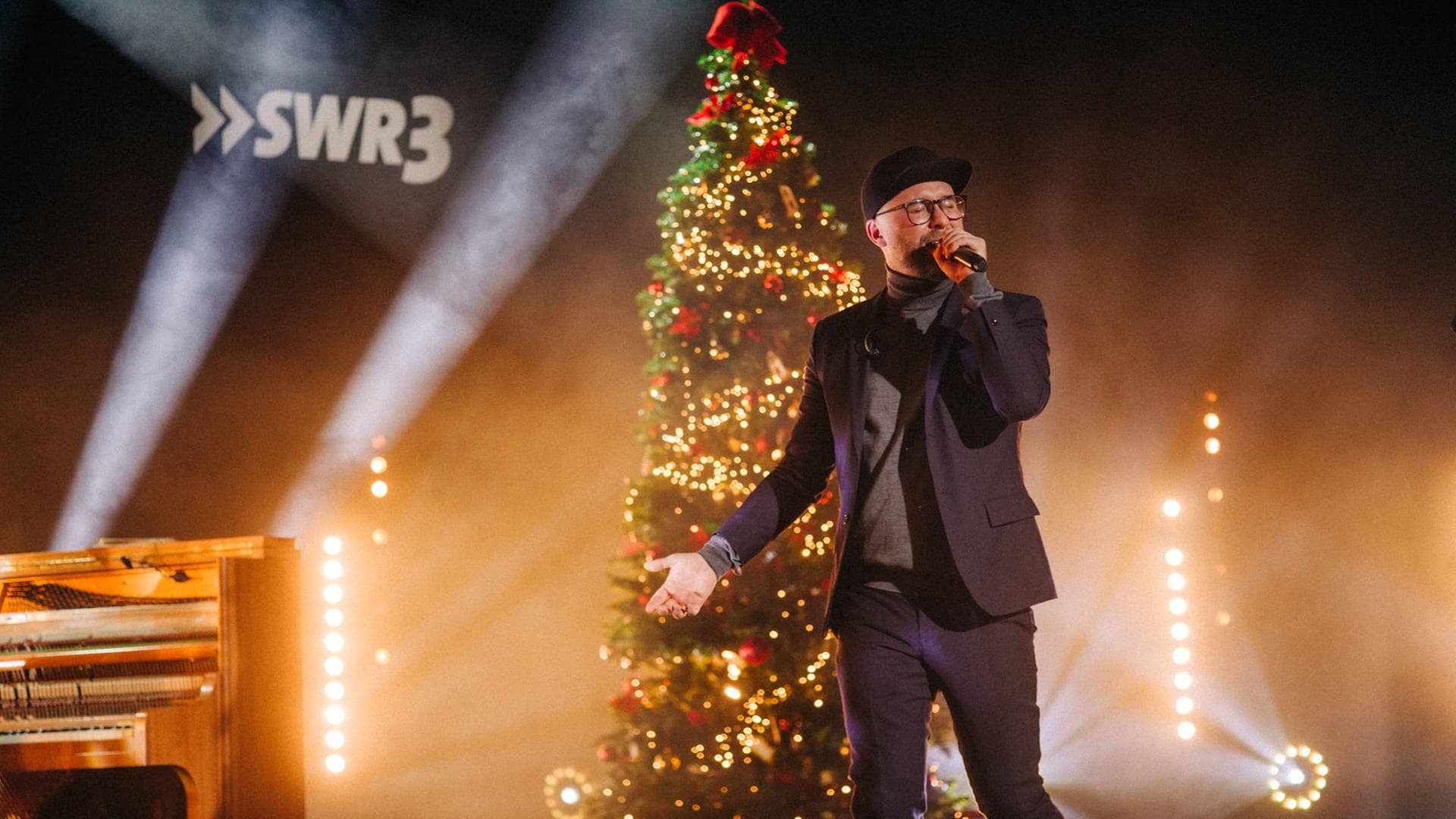 Mark Forster mit Cap und Mikro auf der Bühne vor einem beleuchteten Weihnachtsbaum (Foto: SWR3, SWR3/Niko Neithardt)