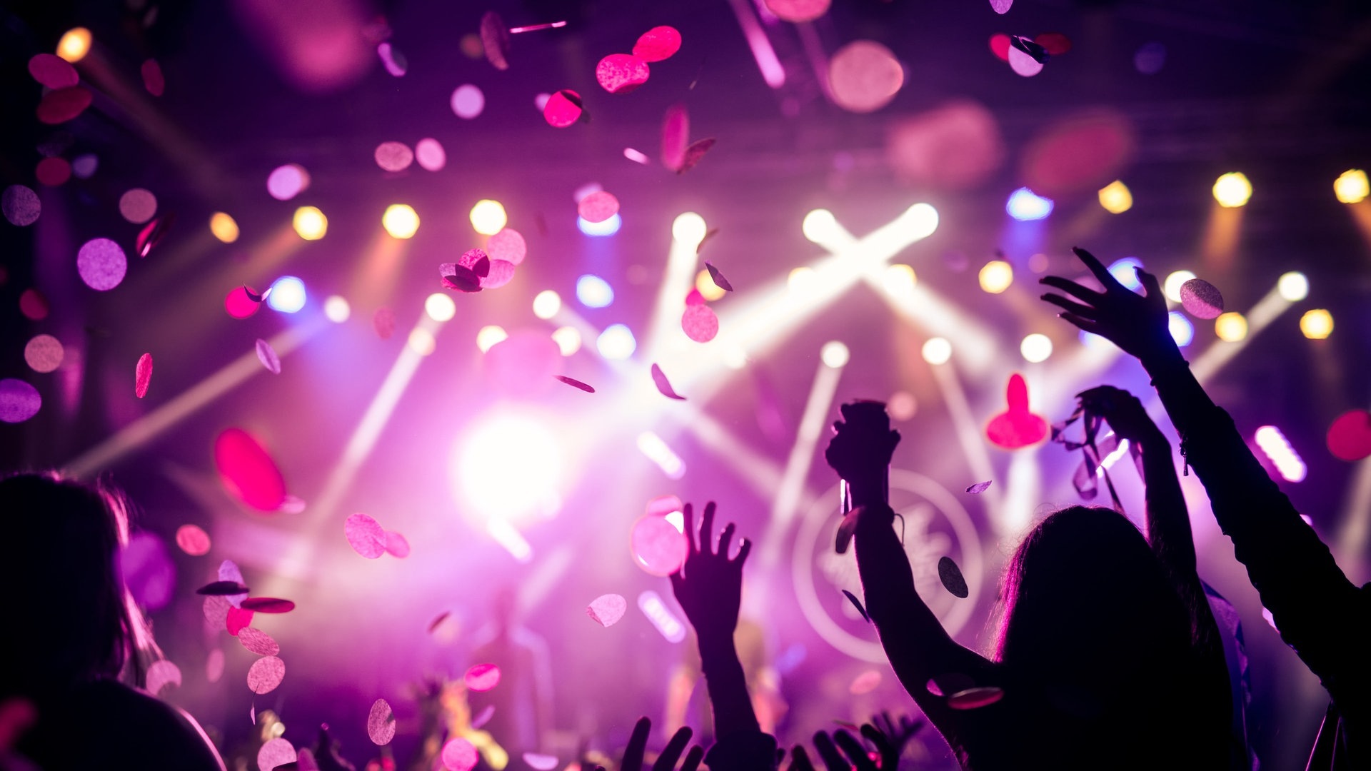 Menschen feiern in einem Raum, der rosa beleuchtet ist und Glitzer von der Decke fällt zur Musik von einem DJ (Foto: Adobe Stock, Adobe Stock // bernardbodo)