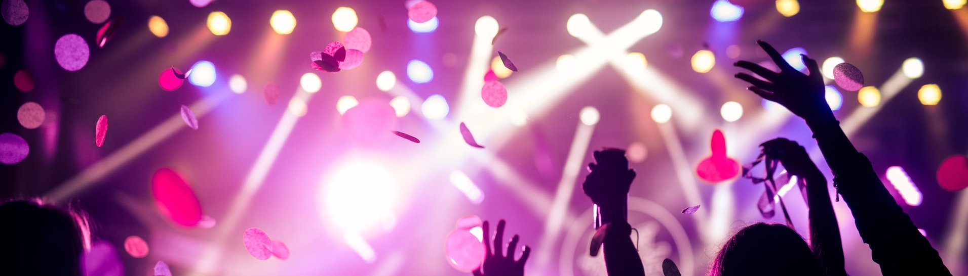 Menschen feiern in einem Raum, der rosa beleuchtet ist und Glitzer von der Decke fällt zur Musik von einem DJ (Foto: Adobe Stock, Adobe Stock // bernardbodo)