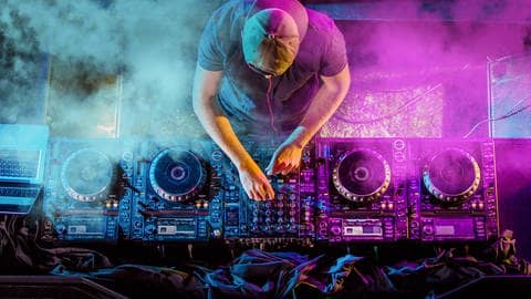 Ein DJ steht am DJ-Pult und es wird gezeigt, wie er Regler bewegt (Foto: Adobe Stock, Adobe Stock // vladimirhodac)