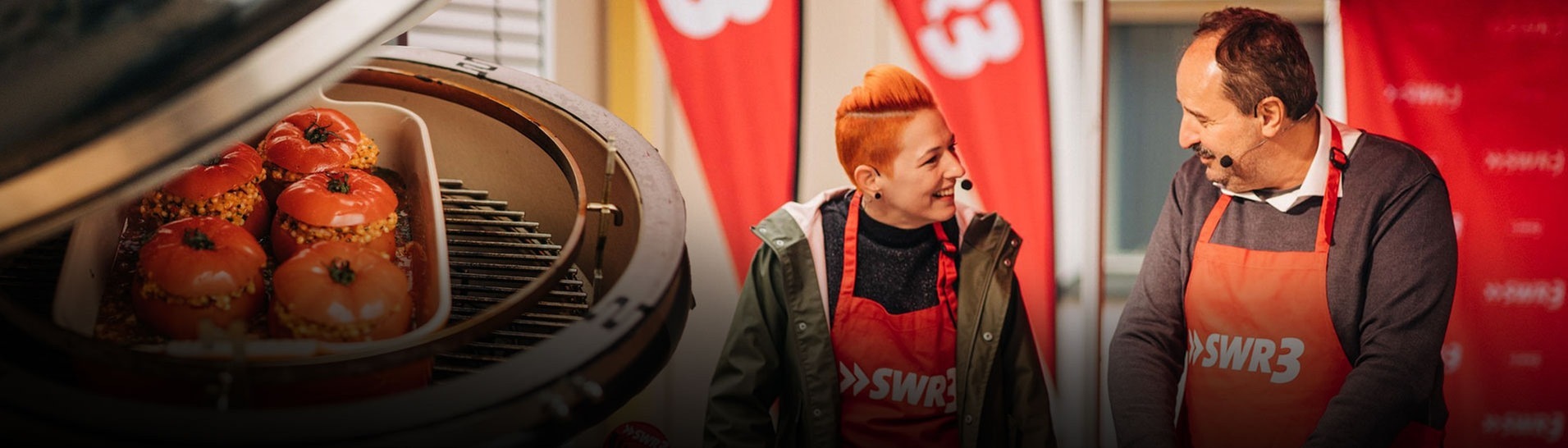 Gefüllte Tomaten auf dem Grill und Meta und Johann im Hintergrund. (Foto: SWR3, Niko Neithardt)