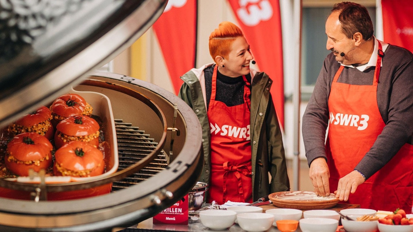 Gefüllte Tomaten auf dem Grill und Meta und Johann im Hintergrund. (Foto: SWR3, Niko Neithardt)