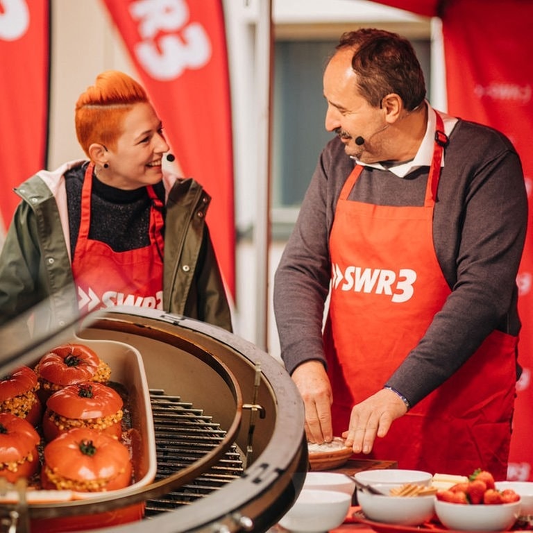 Gefüllte Tomaten auf dem Grill und Meta und Johann im Hintergrund. (Foto: SWR3, Niko Neithardt)